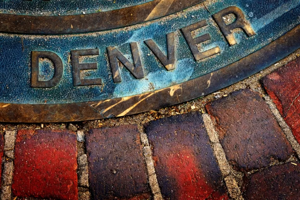 Close-up of Denver title on manhole cover in brick sidewalk or street.